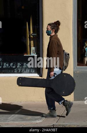 Una giovane donna sulla strada per un evento musicale porta il suo banjo in un caso come lei cammina lungo un marciapiede a Santa Fe, New Mexico. Foto Stock