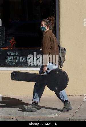 Una giovane donna sulla strada per un evento musicale porta il suo banjo in un caso come lei cammina lungo un marciapiede a Santa Fe, New Mexico. Foto Stock