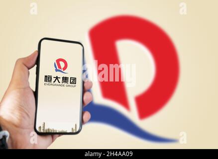 Guangzhou, Cina, Ottobre 2021: Mano che tiene un telefono con il logo Evergrande sullo schermo e il logo sfocato sullo sfondo. Evergrande è il Foto Stock