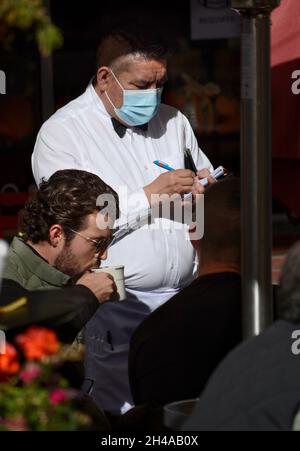Un cameriere che indossa una maschera pandemica porta gli ordini per il pranzo in un ristorante con posti a sedere all'aperto a Santa Fe, New Mexico. Foto Stock