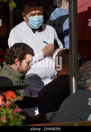 Un cameriere che indossa una maschera pandemica porta gli ordini per il pranzo in un ristorante con posti a sedere all'aperto a Santa Fe, New Mexico. Foto Stock