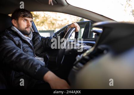 un uomo barbuto è in auto e guarda fuori la finestra. Foto Stock