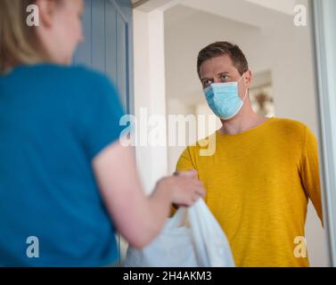 L'uomo mascherato trasporta il cibo durante la pandemia. Foto Stock