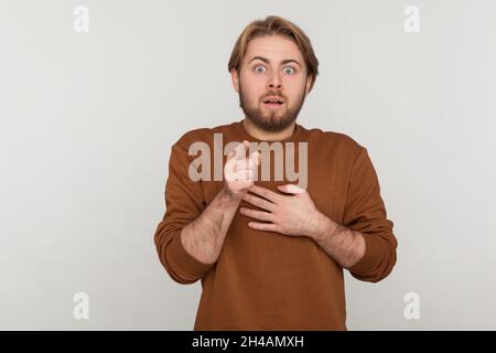 Ritratto di uomo spaventoso con barba che indossa la felpa, che punta alla fotocamera, che guarda confuso paura timido, che indica qualcosa di spaventoso. Studio interno girato isolato su sfondo grigio. Foto Stock