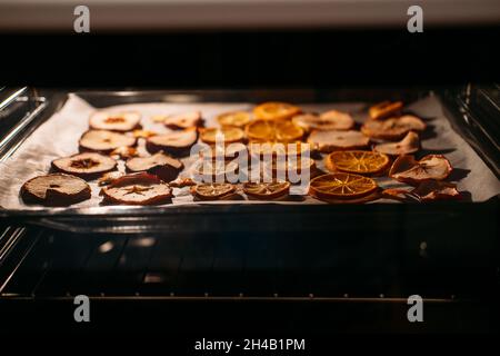 Come asciugare le fette di arancia per decorazione di Natale. Arance che asciugano in forno su griglia metallica e carta da forno. Messa a fuoco selettiva Foto Stock