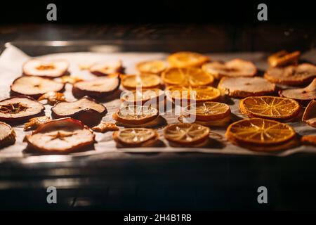 Come asciugare le fette di arancia per decorazione di Natale. Arance che asciugano in forno su griglia metallica e carta da forno. Messa a fuoco selettiva Foto Stock