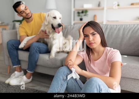 Giovane signora caucasica sensazione di malessere, avendo freddo, tenendo carta tissue, il suo ragazzo arabo con cane da compagnia sullo sfondo, copia spazio. Influenza o coronavirus, Foto Stock
