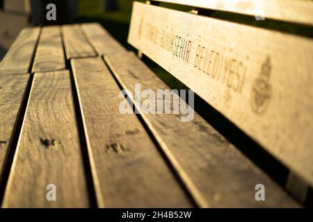 panca di seduta in legno nel parco e silhouette di persone con luce solare Foto Stock