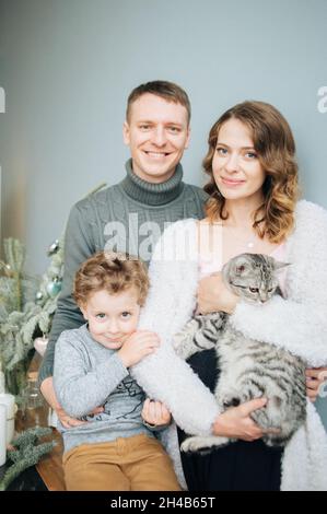Famiglia di tre con gatto guarda una macchina fotografica con sorrisi. Foto Stock