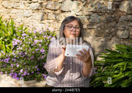 donna più anziana con capelli bianchi con occhiali che guardano il tablet nel parco Foto Stock