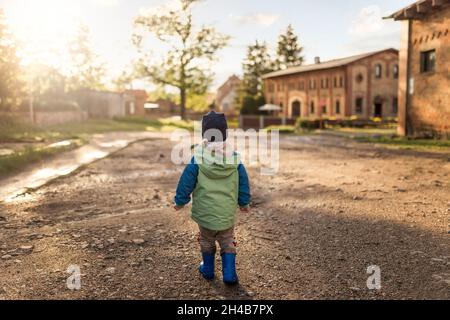 Vista posteriore del ragazzino che cammina su countryRoad e guarda avanti Foto Stock