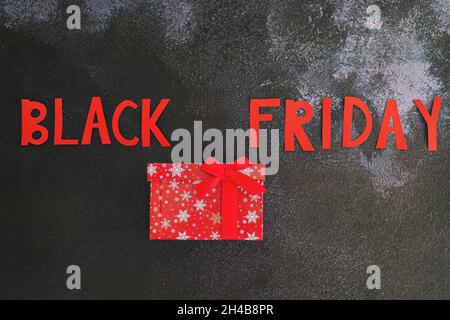 Concetto di Black Friday. Iscrizione "Black friday", confezione regalo rossa su sfondo nero. Spazio di copia, vista dall'alto, disposizione piatta. Volantino vacanza creativo. Vendita. Foto Stock