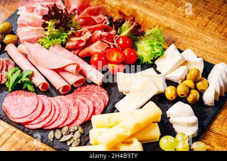 Salumi, antipasti con assortimento di salumi, formaggi, camembert e olive su tavola di legno. Vari tipi di carne e salsicce su legno Foto Stock