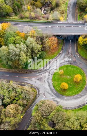 Vista aerea del drone di una piccola rotatoria con alberi che mostrano colori autunnali (Galles, Regno Unito) Foto Stock