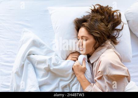 Vista dall'alto: Una giovane donna dorme abbracciando una coperta. Il concetto di recupero e di sonno sano. Foto Stock