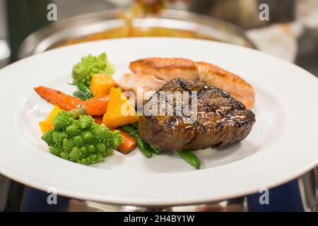 Viene preparato un piatto con bistecca, salmone alla griglia, purè di patate e verdure arrostite. Foto Stock