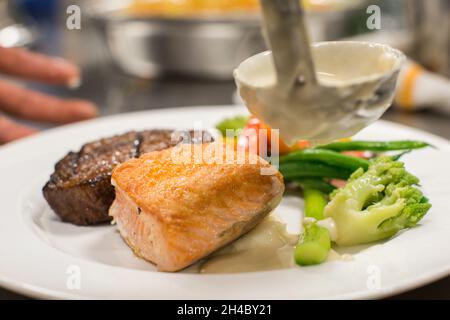 Viene preparato un piatto con bistecca, salmone alla griglia, purè di patate e verdure arrostite. Foto Stock