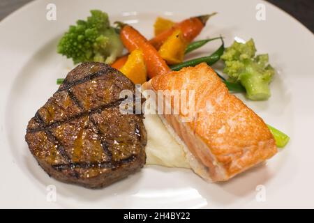 Viene preparato un piatto con bistecca, salmone alla griglia, purè di patate e verdure arrostite. Foto Stock