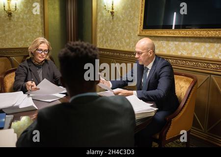 Gruppo di avvocati interculturali contemporanei in abbigliamento formale riuniti da tavolo in elegante sala riunioni di lavoro Foto Stock