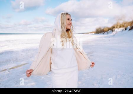 Donna felice di mezza età che indossa bianco clotheswalk da solo lungo la spiaggia di mare d'inverno o oceano e respirare con aria fresca fredda Foto Stock