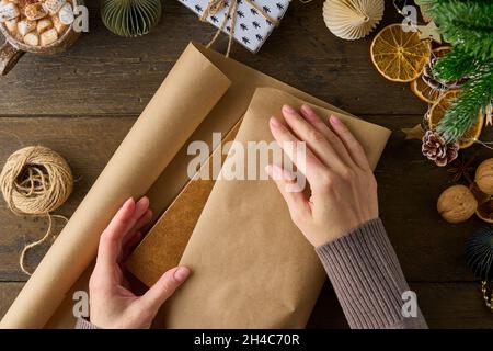 Donna irriconoscibile imballaggio regali di natale su tavola di legno. Decorazioni di Capodanno Foto Stock