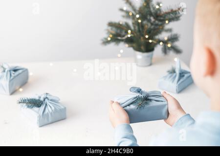 Una mano del bambino che tiene il pacchetto eco-friendly del tessuto riutilizzabile su un tavolo bianco. Senza plastica. Stile di vita senza sprechi. Foto di alta qualità Foto Stock