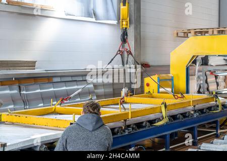 Deposito di prodotti finiti. Nastro trasportatore o linea con tegole metalliche confezionate all'interno dell'officina mediante gru. Produzione industriale di coperture su attrezzature automatizzate. Foto Stock