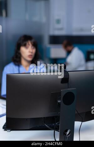 Primo piano della webcam sul moderno computer per videochiamate e comunicazioni remote in ufficio. Infermiera che utilizza la telecamera sul monitor per videoconferenze e telemedicina online, lavorando a tarda notte. Foto Stock