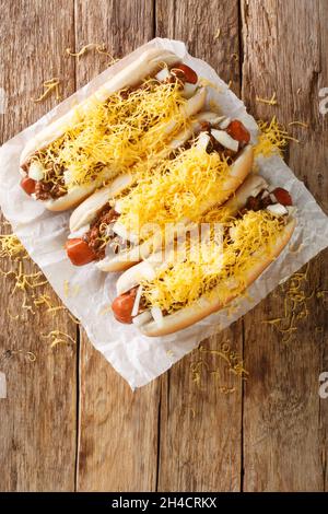 Cincinnati fast food hot dog al peperoncino con salsiccia di manzo, formaggio cheddar e cipolle da vicino su un vecchio sfondo di legno. Vista dall'alto verticale Foto Stock