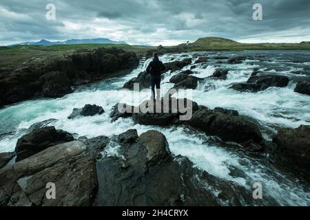 Emozioni accanto ad una cascata in Islanda, natura selvaggia e forte, ragazzo è in piedi sopra la cascata e ha le mani estese Foto Stock