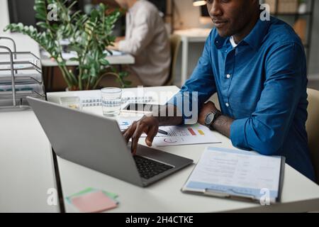 Scatto corto del giovane uomo afroamericano che usa il laptop alla scrivania mentre lavora in ufficio Foto Stock