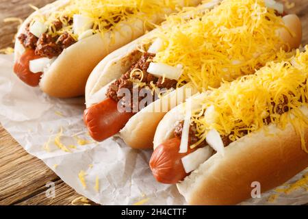 Hot dog di manzo in una pistola coperta con Cincinnati Chili, cipolle a dadini, e un cumulo di formaggio cheddar grattugiato closeup nella carta sul tavolo. Horizonta Foto Stock