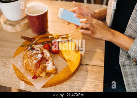 Una ragazza è seduta ad un tavolo e testando sul suo smartphone in una cafe.A ragazza è seduta in un bar con un telefono.scrive nel telefono. Foto Stock