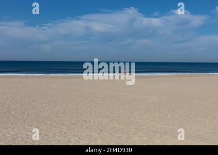 Leerer Strand mit rotem Sonnenschirm und zwei Strandbesuchern, nicht erkennbar) in Espinho Foto Stock