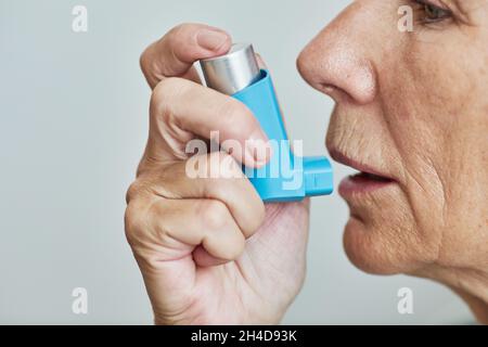 Primo piano della vista laterale minima della donna anziana che usa l'inalatore contro il bianco, spazio di copia Foto Stock