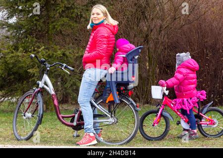 Bambino in sella donna in bicicletta e due bambini Foto Stock