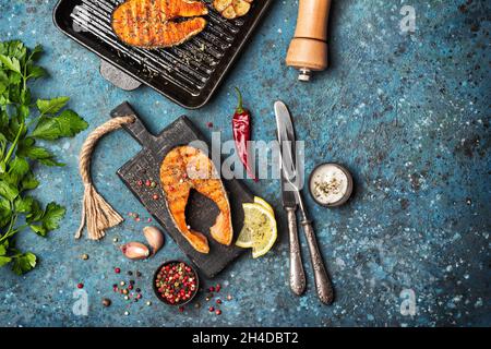 Vista dall'alto della bistecca di salmone di pesce rosso alla griglia su padella di ghisa o padella con spezie, aglio fritto, limone, prezzemolo, pephreb e gustosa salsa di coco blu Foto Stock