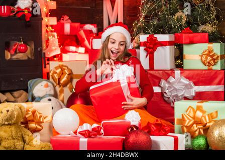 Bambino piccola ragazza felice trovare i regali vicino albero di natale. Buon Natale. Concetto di infanzia felice. Scopri la bellezza dell'inverno. Capretto santa cappello di natale Foto Stock