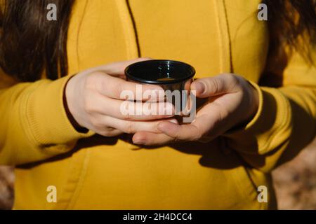 Una donna tiene una tazza termica di tè nella foresta autunnale, mani da vicino Foto Stock