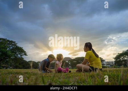 Madre e i suoi bambini giocano sul campo da calcio verde all'ora del tramonto. Concetto di famiglia amichevole. Foto Stock