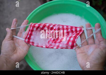 Donna mano lavatrice una maschera con detergente sciolto in acqua. Il lavaggio delle maschere sta disinfettando e risparmiare denaro per essere utilizzato di nuovo. Foto Stock