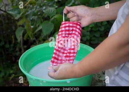 Donna mano lavatrice una maschera con detergente sciolto in acqua. Il lavaggio delle maschere sta disinfettando e risparmiare denaro per essere utilizzato di nuovo. Foto Stock