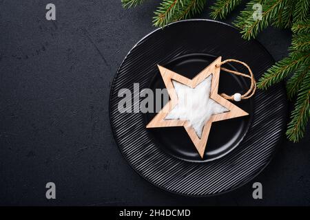 Servito tavolo di natale impostazione vuoto nero piastra di ceramica su sfondo scuro. Decorazione di Natale. Decorazioni per le vacanze con stella in legno e ramo in abete Foto Stock