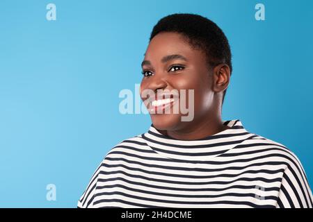 Ritratto di allegra Signora Africana in sovrappeso guardando da parte, sfondo blu Foto Stock