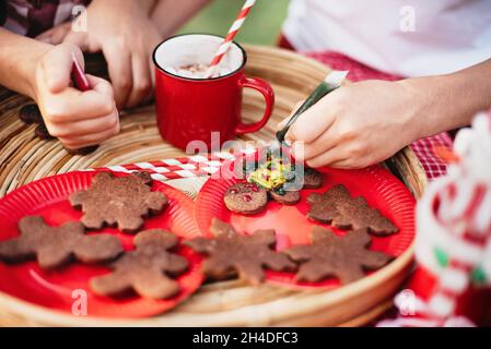 Bambini felici che si preparano per Natale. Due ragazzi e bambina in biscotti di pan di zenzero di colore santa Hat, bevendo cioccolata calda fuori divertirsi. Deco bambini Foto Stock