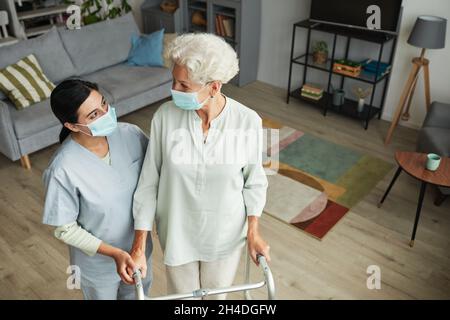 Ritratto ad angolo alto di sorridente infermiere donna che aiuta anziana con mobilità walker in casa di riposo, copia spazio Foto Stock