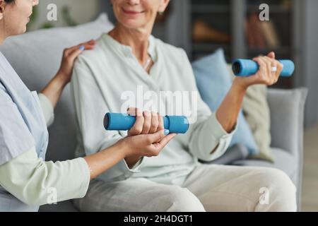 Primo piano di sorridente formazione donna anziana con pesi in pensione casa, copia spazio Foto Stock