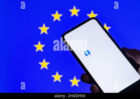 Vilnius Lituania 01 NOV 2021 Silhouette di uomo mano tenere smartphone con Facebook app mostrato su schermo bianco in sfocato Unione europea bandiera backgro Foto Stock