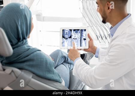 Dentista maschio arabo che mostra i denti X-ray su tavoletta digitale a femmina musulmana Foto Stock