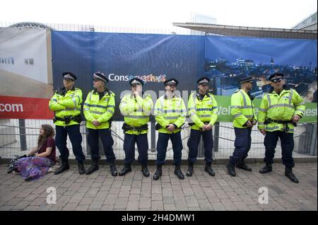 La polizia si trova al di fuori del centro convegni centrale di Manchester, come dimostrano gli attivisti anti-governativi nel terzo giorno della conferenza annuale del partito conservatore a Manchester. Foto Stock